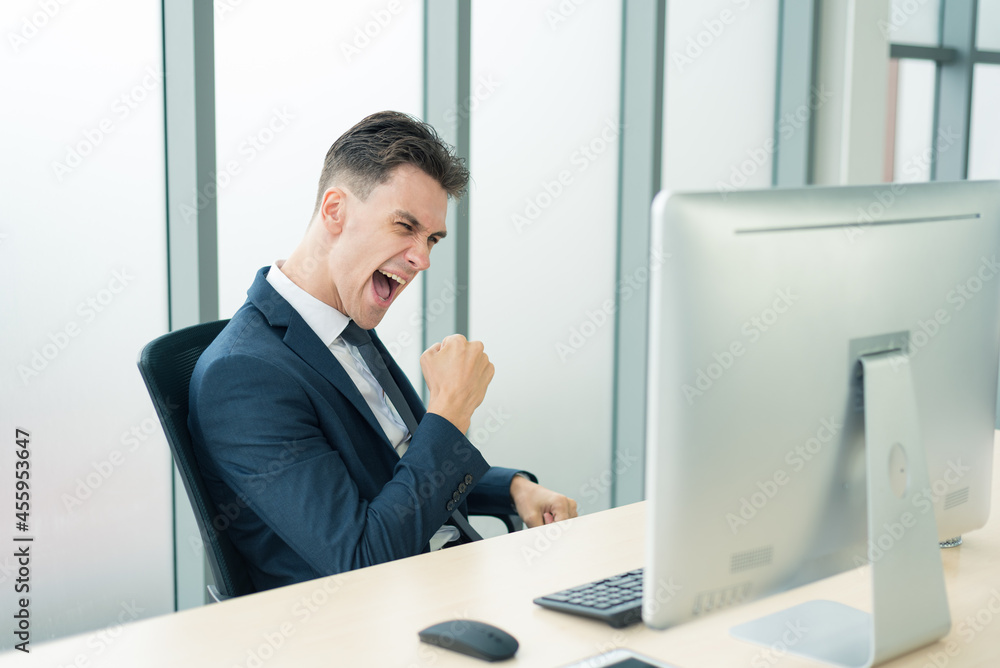 Portrait of smart confident business man in suit outfit sitting in front of computer and acting extremely success from work in modern office room Portrait of smart confident business man in suit outfit sitting in front of computer and acting extremely success from work in modern office room