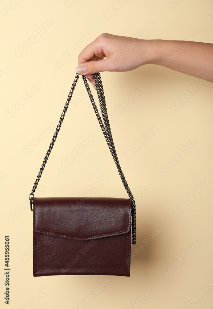 Woman holding stylish bag on beige background, closeup