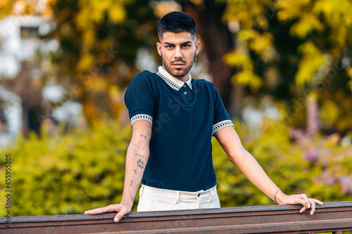 Portrait if a man with modern clothes and tattoos leaning on a rail in a park © Samuel Perales