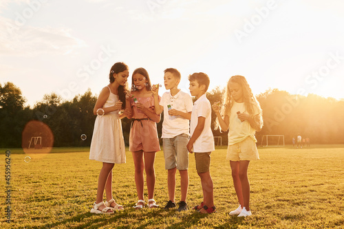 Illuminated by sunlight. Standing on the sportive field. Group of happy kids is outdoors at daytime © standret