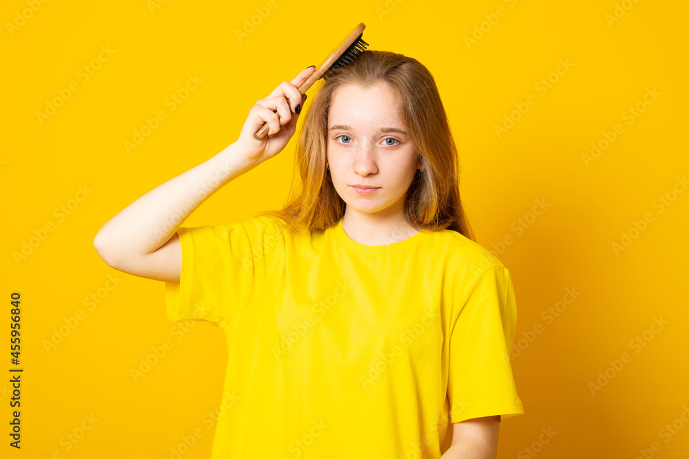 Cute blond hair teen girl, combing hair with wooden brush on yellow background. Cute blond hair teen girl, combing hair with wooden brush on yellow background.