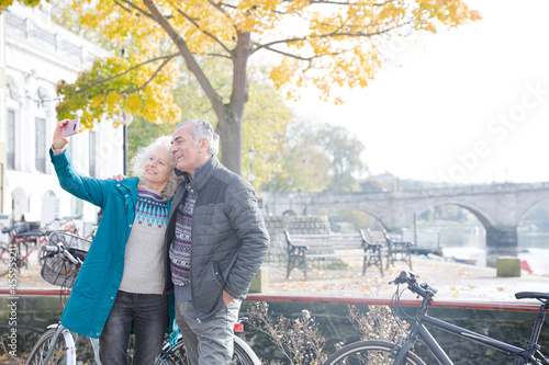 Senior couple with bicycles taking selfie at autumn river