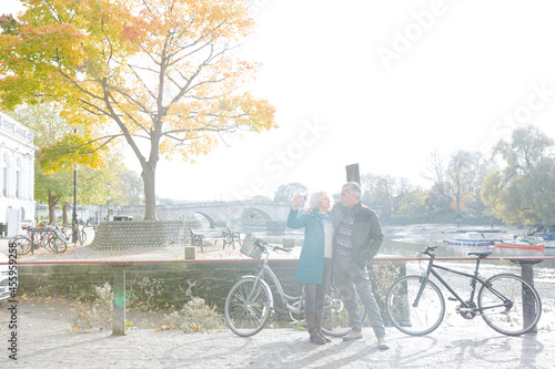 Senior couple with bicycles taking selfie at autumn river
