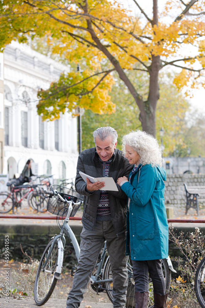 Senior couple with bicycles traveling, looking at guidebook along autumn river