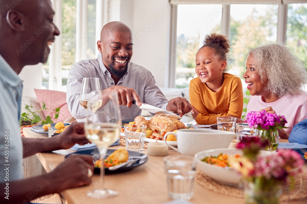 Father Carving As Multi Generation Family Sit Around Table At Home And Enjoy Eating Meal Father Carving As Multi Generation Family Sit Around Table At Home And Enjoy Eating Meal
