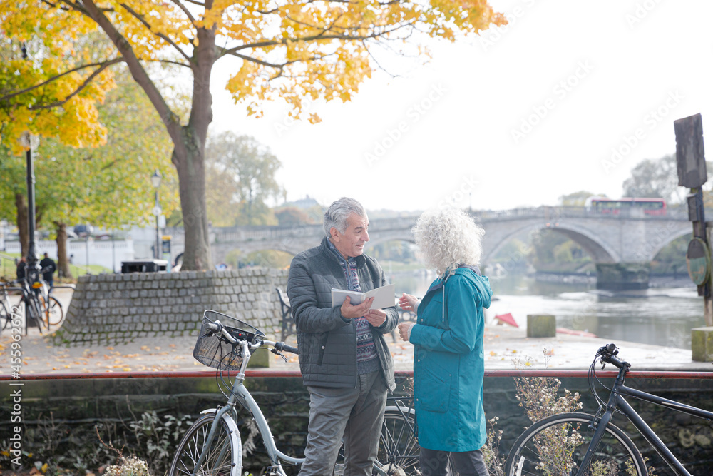 Obraz premium Senior couple with bicycles traveling, looking at guidebook along autumn river