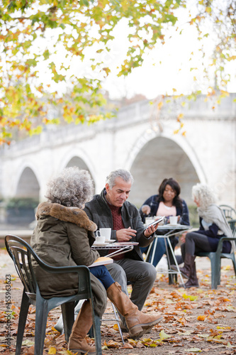 Senior couple using digital tablet, enjoying coffee and tea at autumn park