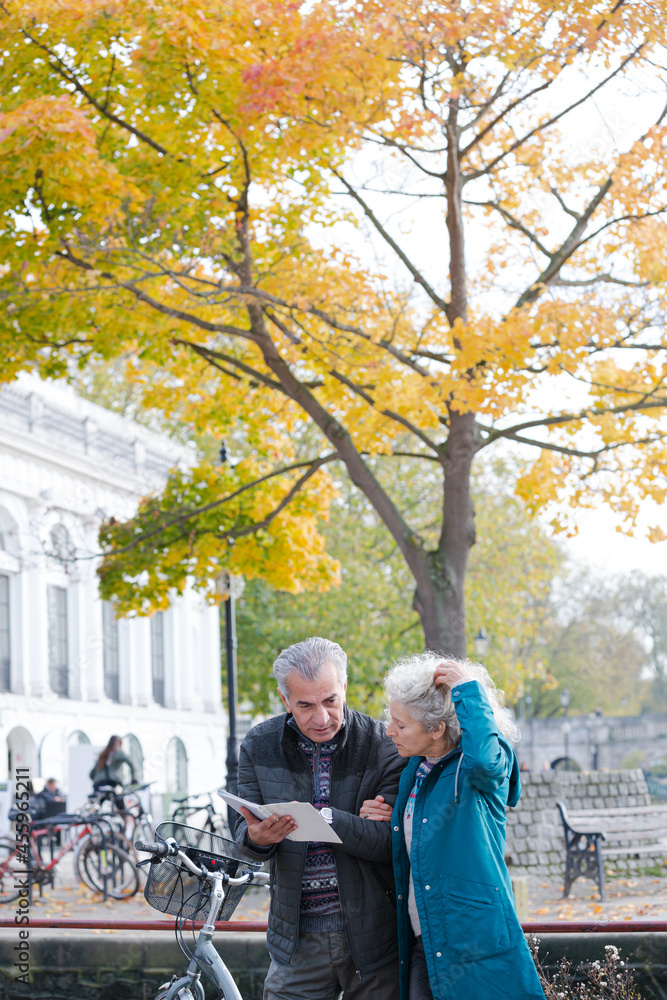 Obraz premium Senior couple with bicycles traveling, looking at guidebook along autumn river