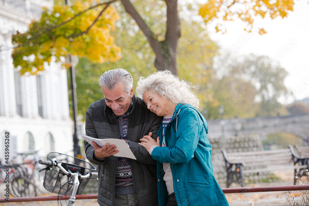 Senior couple with bicycles traveling, looking at guidebook along autumn river