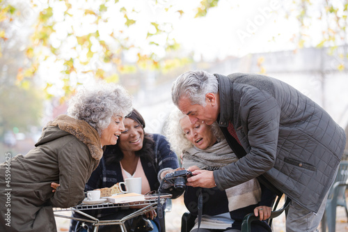 Active senior friends using digital camera at autumn sidewalk cafe