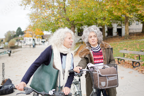 Smiling active senior women walking bicycles in autumn park