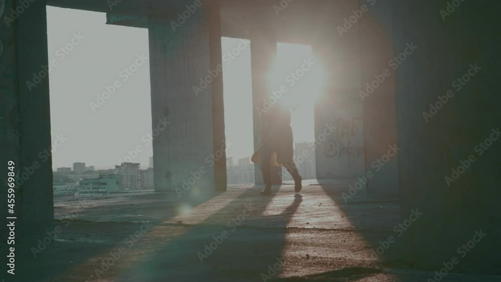 man in protective suit, gas mask, with weapon, runs through an unfinished building against backdrop of bright sun and city high-rise buildings. Atmosphere of post-apocalypse, pandemic. man in protective suit, gas mask, with weapon, runs through an unfinished building against backdrop of bright sun and city high-rise buildings. Atmosphere of post-apocalypse, pandemic.