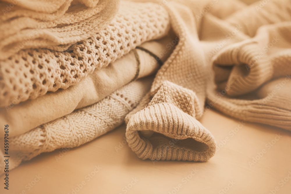 Fototapeta premium Delicate soft cozy beige wool sweaters are stacked in a pile and illuminated by sunlight. Clothing for the season. Autumn cold weather.