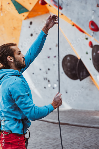 Young man professional rock climber checking sports equipment before climbing at training center in sunny day, outdoors. Concept of healthy lifestyle, activity