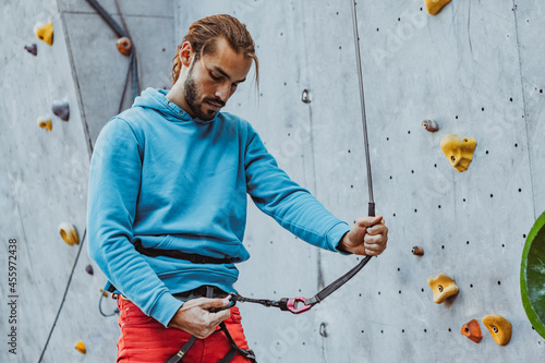 Safety climbing. Young man professional rock climber checking sports equipment before climbing at training center in sunny day, outdoors. © master1305
