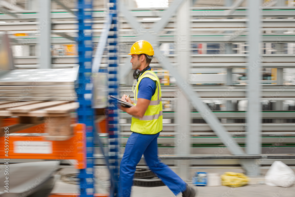 Factory worker with clipboard inspecting steel parts in factory Factory worker with clipboard inspecting steel parts in factory