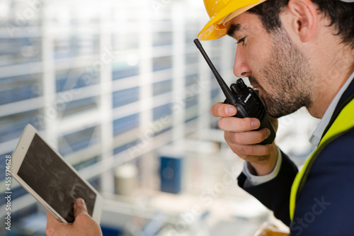 Male supervisor with digital tablet talking, using walkie-talkie on platform in factory