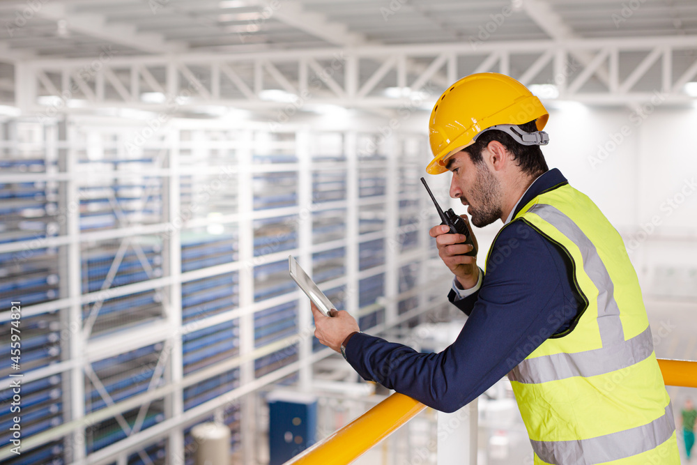 Male supervisor with digital tablet talking, using walkie-talkie on platform in factory Male supervisor with digital tablet talking, using walkie-talkie on platform in factory