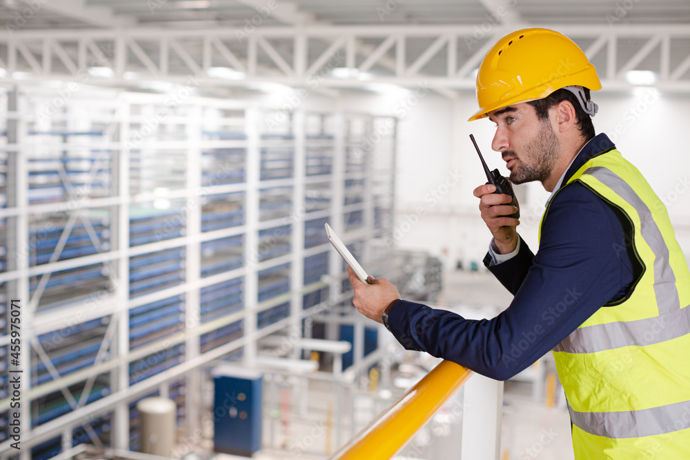 Male supervisor with digital tablet talking, using walkie-talkie on platform in factory Male supervisor with digital tablet talking, using walkie-talkie on platform in factory