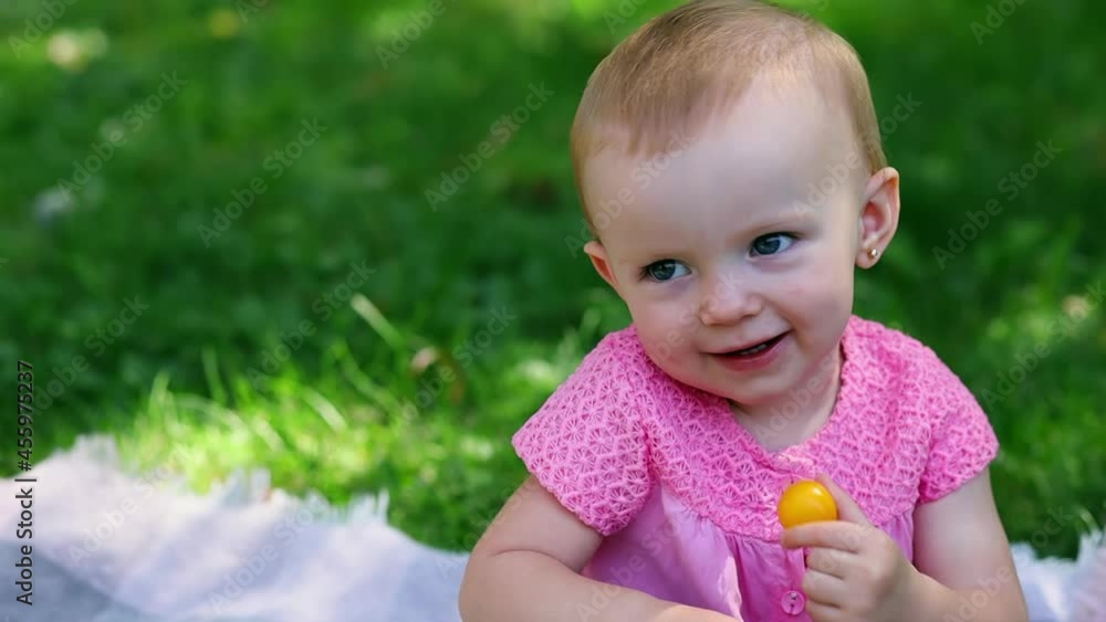 A happy little girl is sitting on the grass and holding a yellow cherry plum in her hands A happy little girl is sitting on the grass and holding a yellow cherry plum in her hands