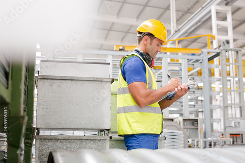 Factory worker with clipboard inspecting steel parts in factory