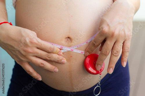 Close up of a pregnant woman measuring her belly with a tape. Centimeter measurement. Man measuring his wife belly with a tape.