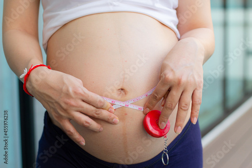 Close up of a pregnant woman measuring her belly with a tape. Centimeter measurement. Man measuring his wife belly with a tape.