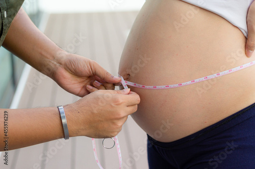 Man measuring his wife belly with a tape. Close up of a pregnant woman measuring her belly with a tape. Centimeter measurement.