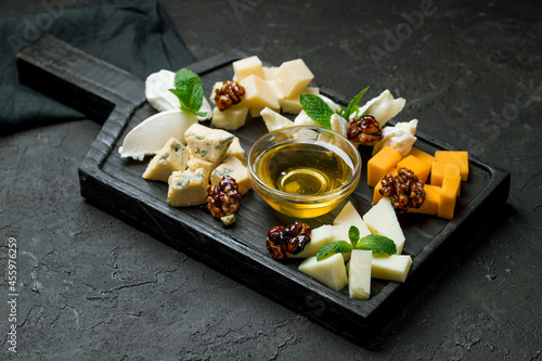 assorted European cheeses on black board with honey and walnuts on dark stone table