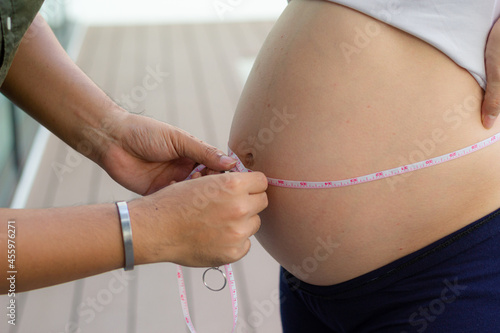 Man measuring his wife belly with a tape. Close up of a pregnant woman measuring her belly with a tape. Centimeter measurement.