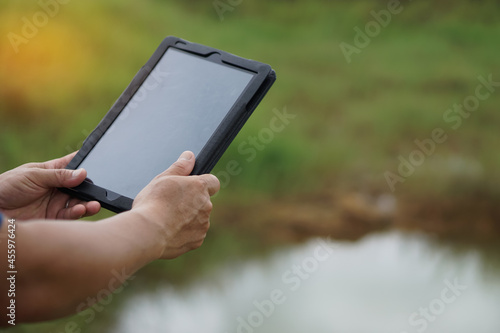 Concept : Wireless internet access technology smart device everywhere. Hands holds smart tablet beside the pond in rural area.                   