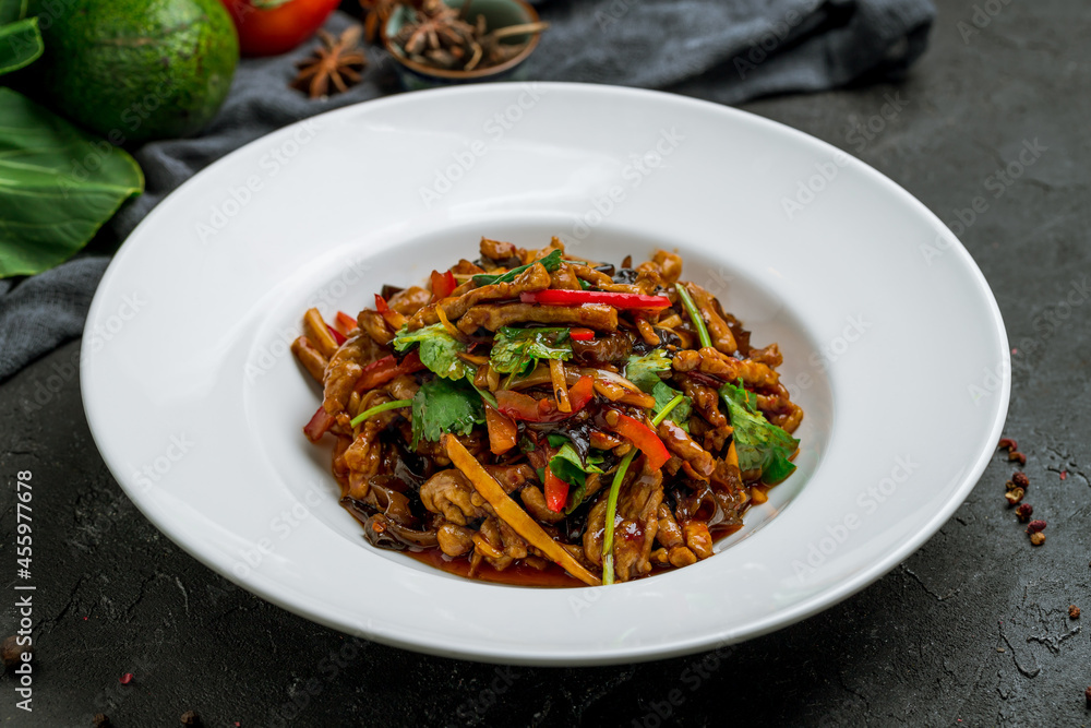 aromatic roast sliced pork with vegetables in hot sauce on white plate on dark stone table aromatic roast sliced pork with vegetables in hot sauce on white plate on dark stone table