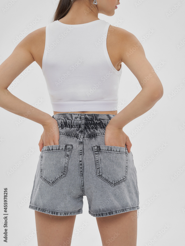 © Dmitry Tsvetkov - Young elegant stylish woman with long brunette hair and natural make-up in white top, grey shorts and slippers posing against bright grey background