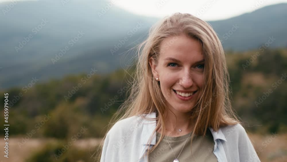 Young smiling blonde woman standing in mountains, portrait Young smiling blonde woman standing in mountains, portrait