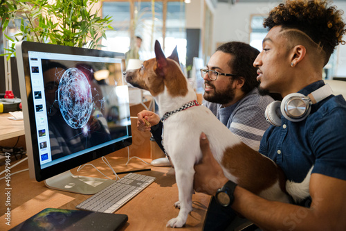 Man holding dog, sitting at computer with colleague photo