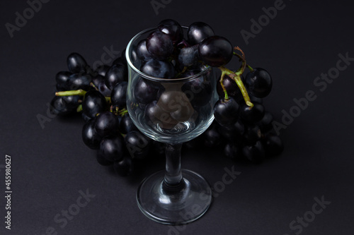 Black grapes on a black background. A bunch of grapes next to an empty glass on a dark background