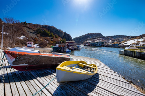 Multiple small white and grey color open wooden fishing boats or dories lined up on a wooden slipway with a bright red fishing shed and white color houses at the top of the slipway.  photo