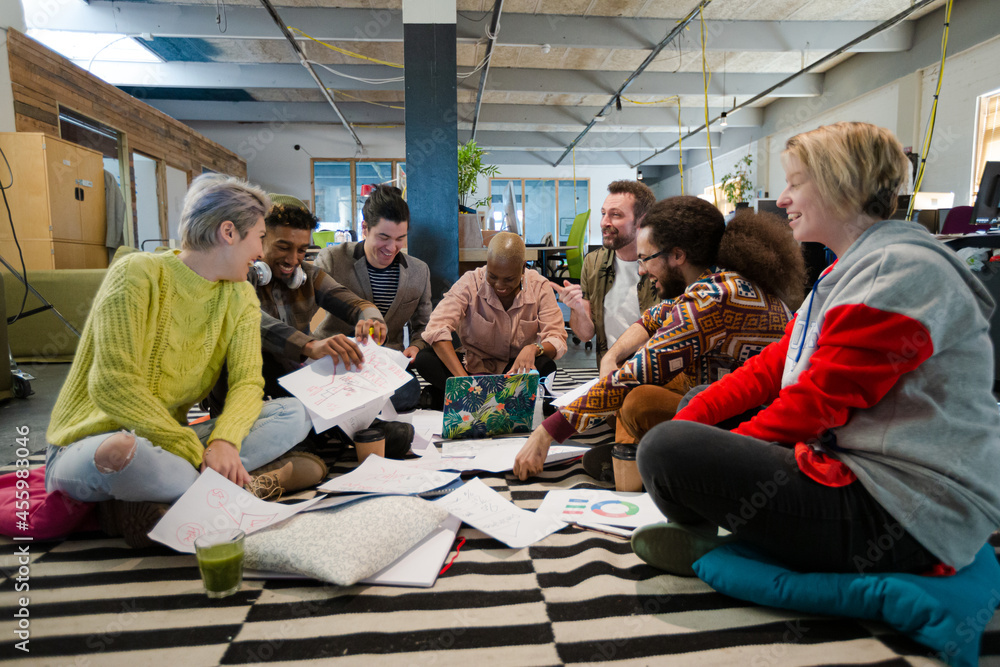 Team sitting on office floor, discussing paperwork Team sitting on office floor, discussing paperwork