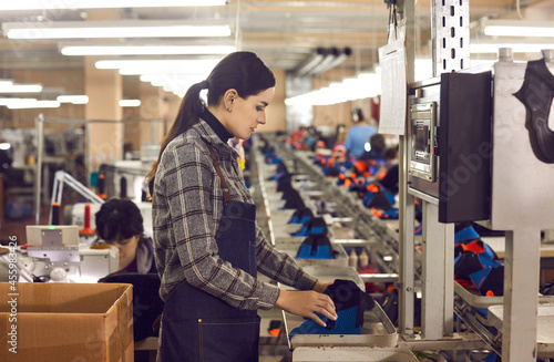 Concentrated young female manufacturing workshop worker making shoe at mass production line of footwear factory. Woman shoemaker using machine equipment. Profession and industry concept
