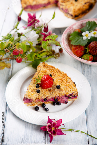 Slice of strawberry and blueberry pie on white wooden table.