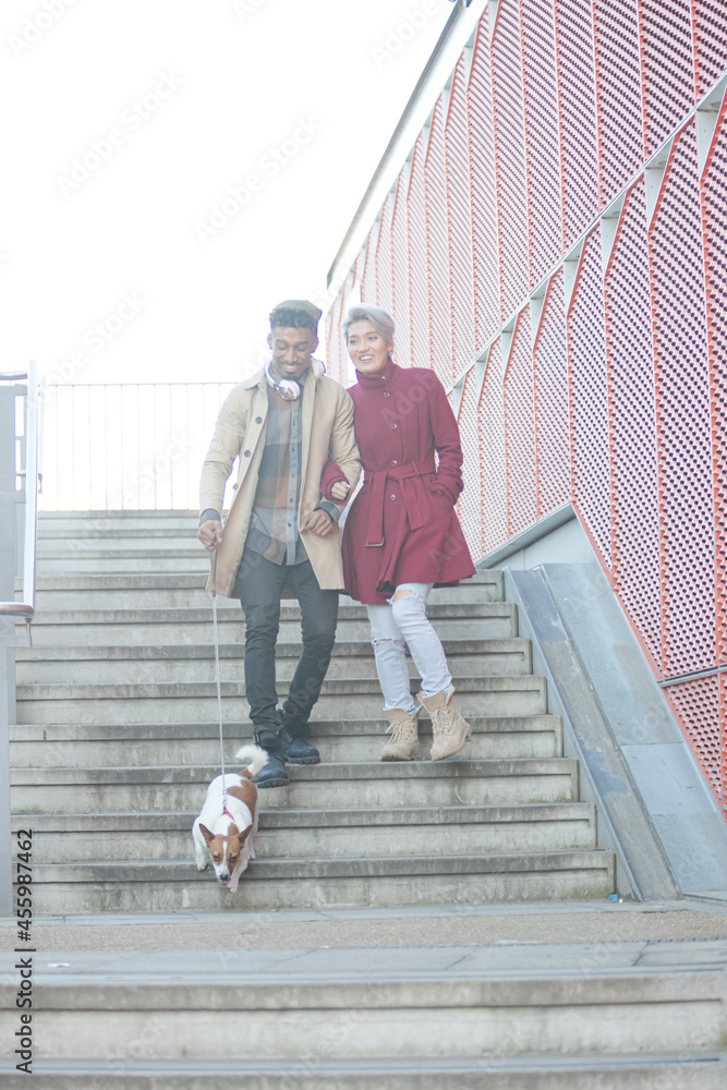 Smiling young couple walking dog down urban, modern stairs