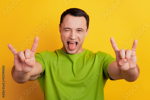 Portrait of funny guy show horns rock gesture stick out tongue on yellow background © Tetiana