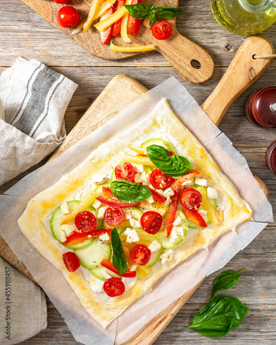 The process of making a puff pastry pie with a vegetable mixture and mozzarella cheese on a serving board on a culinary background closeup. Raw dough and baking ingredients on the table