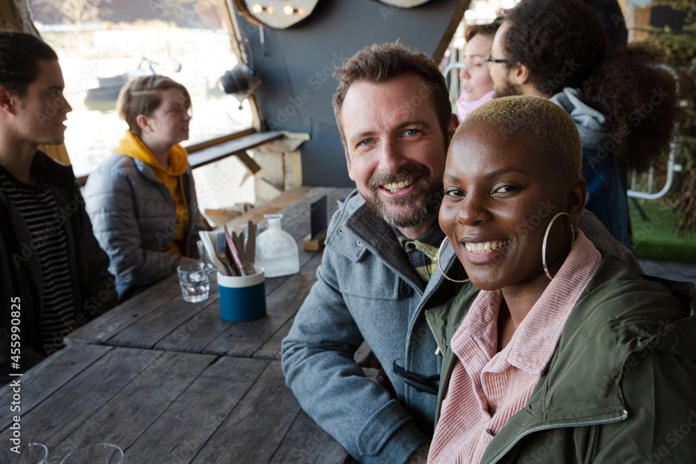 Obraz premium Portrait of smiling couple dining with friends at restaurant outdoor patio