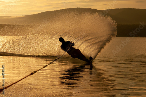 Silhouette of a Man practicing water ski slalom at a lake in the sunrise sunset making water spray in mexico