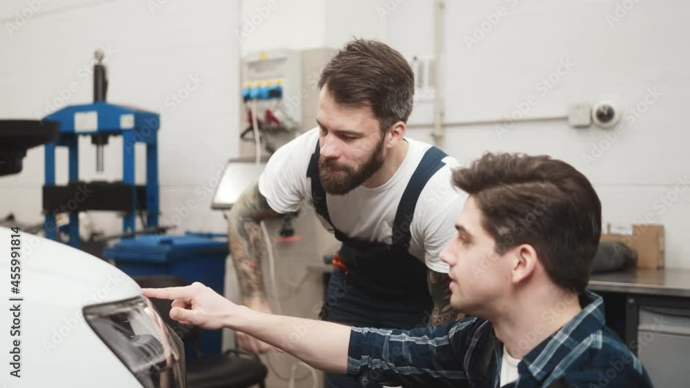 Confident auto mechanics men fixing car while working in garage indoors Confident auto mechanics men fixing car while working in garage indoors