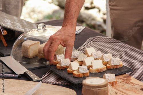 Mr. takes slice of bread with cheese from a cheese board to taste