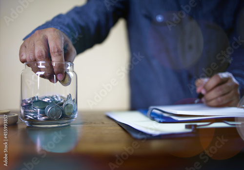 Asian businessmen are calculating costs and profits after trading and dropping coins in a glass jar for savings. Financial and accounting concept.