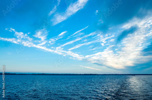 River landscape. Calm water and beautiful blue sky with clouds. Trees grow on the nearest shore. There is copy space