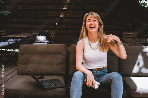 Portrait of a young beautiful woman sitting with a laptop and a phone on the sofa in a cozy work area